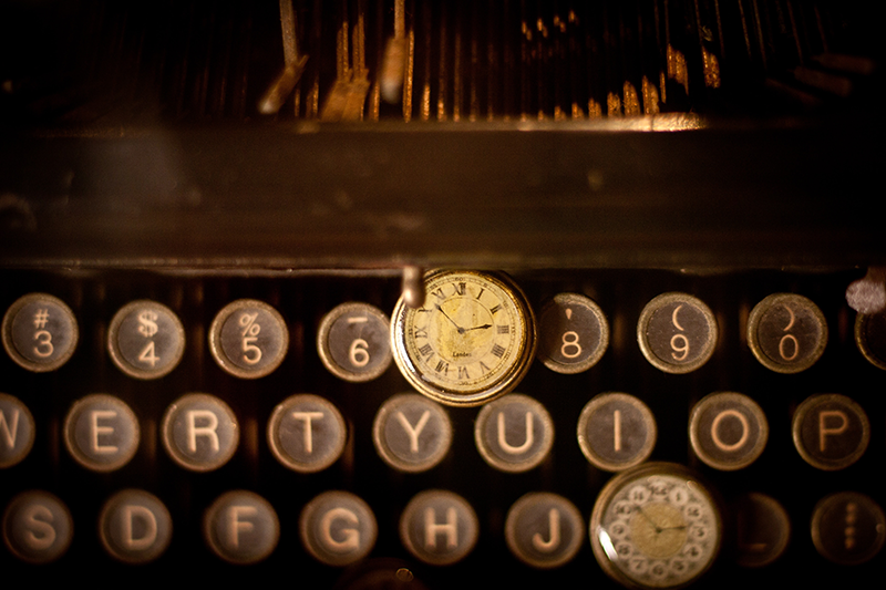 Old typewriter with a time piece draped over it.